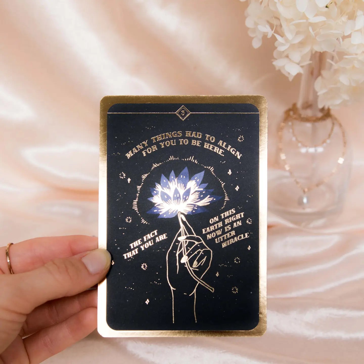 Soul Whispers Gold Foiled 33 Card Deck featuring a beautifully designed card with a hand holding a lotus flower
