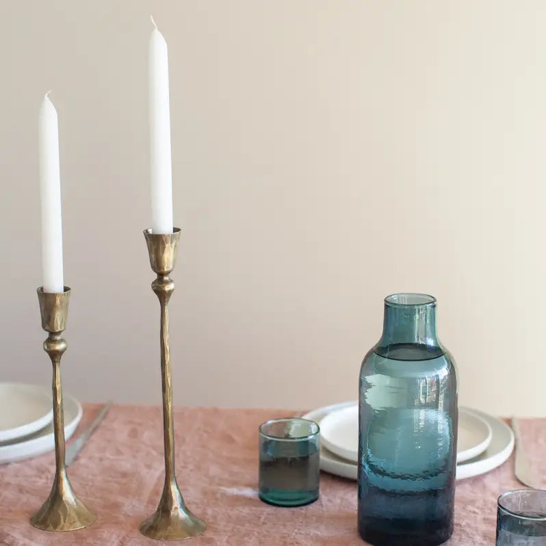 Vintage style metal candlesticks with white candles set on a dining table with blue glassware